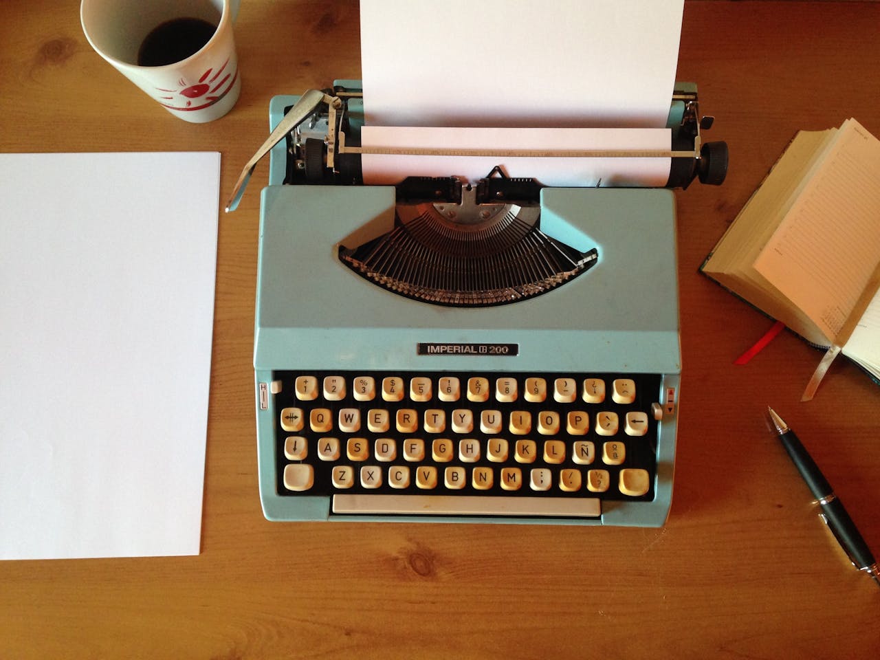 Classic blue typewriter on a wooden desk with paper, pen, and notepad, evoking vintage nostalgia.